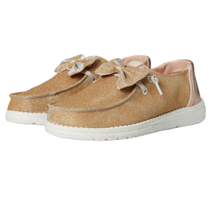 Hey Dude Wendy Sparkle Bow Shoes are slip-on shoes featuring a shimmer gold fabric, decorative bow, and a cushioned white sole for comfort.