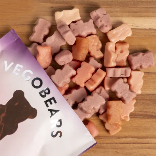 10pk Organic Gummy Bears feature soft, bear-shaped gummies in pastel colors, spilling from a partially visible purple and white package labeled \“VEGOBEARS.\“