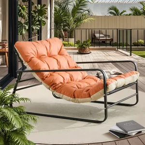 A cushioned lounger with a black metal frame and orange padding is placed on a deck surrounded by greenery, next to a stack of books.