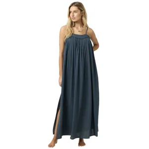 A woman wearing a long, dark blue maxi dress with thin straps, a gathered bodice, and a side slit. She stands barefoot, adding a casual and relaxed appearance.