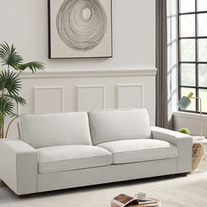 A modern light gray chenille sofa measuring 88.5 inches, featuring clean lines and two large seat cushions. It's set against a white paneled wall with a circular abstract artwork above it. A plant and a window with gray curtains complete the setting.
