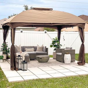 A gazebo with a fabric canopy and curtains over a patio seating set, accompanied by decorative lanterns and potted plants.