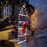 Festive balcony decoration featuring a Santa figure climbing a lighted ladder, adorned with string lights and greenery with red ornaments.