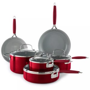 A set of red cookware with two pots, two pans, and corresponding glass lids, all featuring matching red handles.