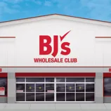 BJ's Wholesale Club storefront featuring signs for curbside pickup and a spirits shop, set against a clear blue sky.