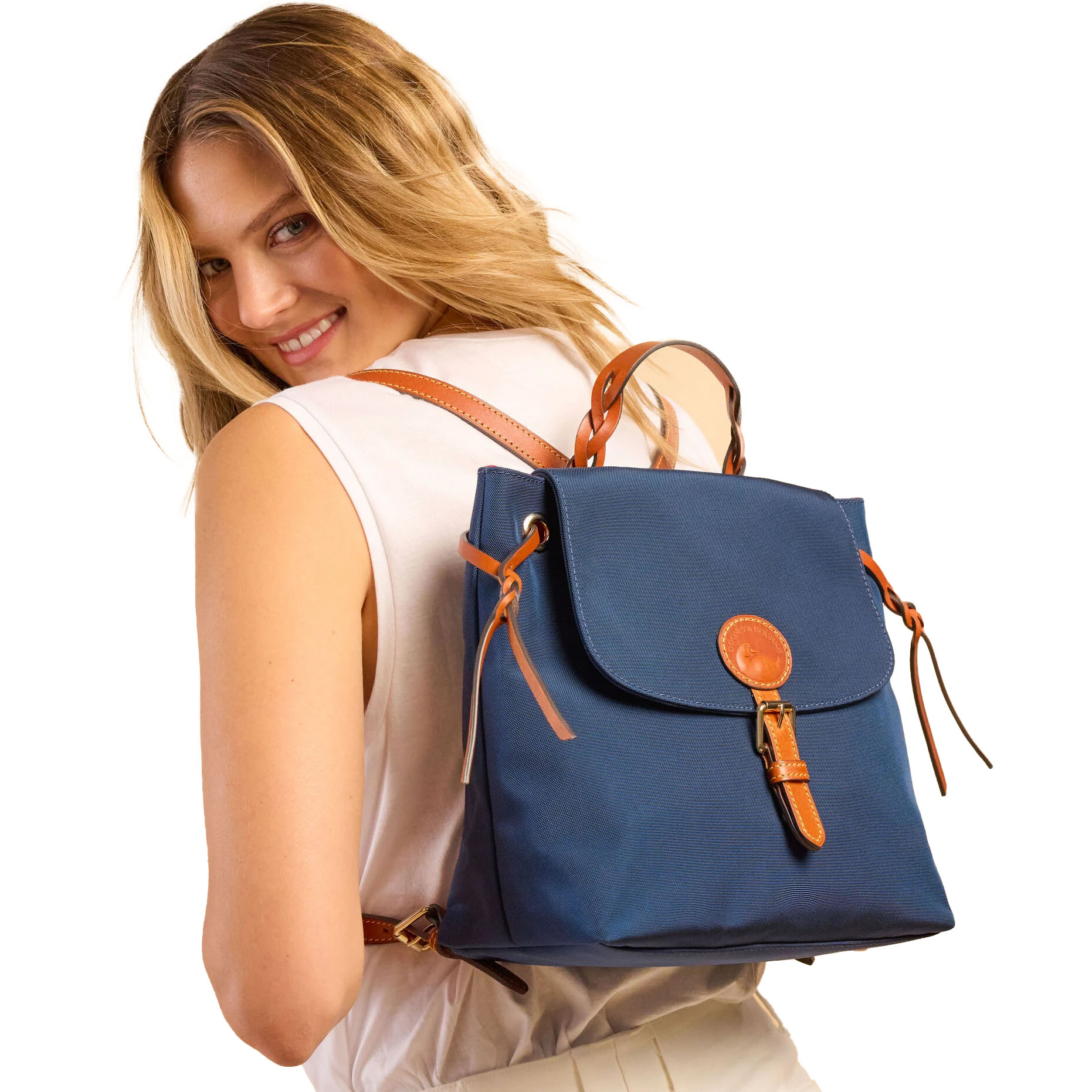 A navy blue Dooney & Bourke backpack with tan leather accents features a front flap secured by a leather strap and brass buckle, complete with a top handle and adjustable shoulder straps.