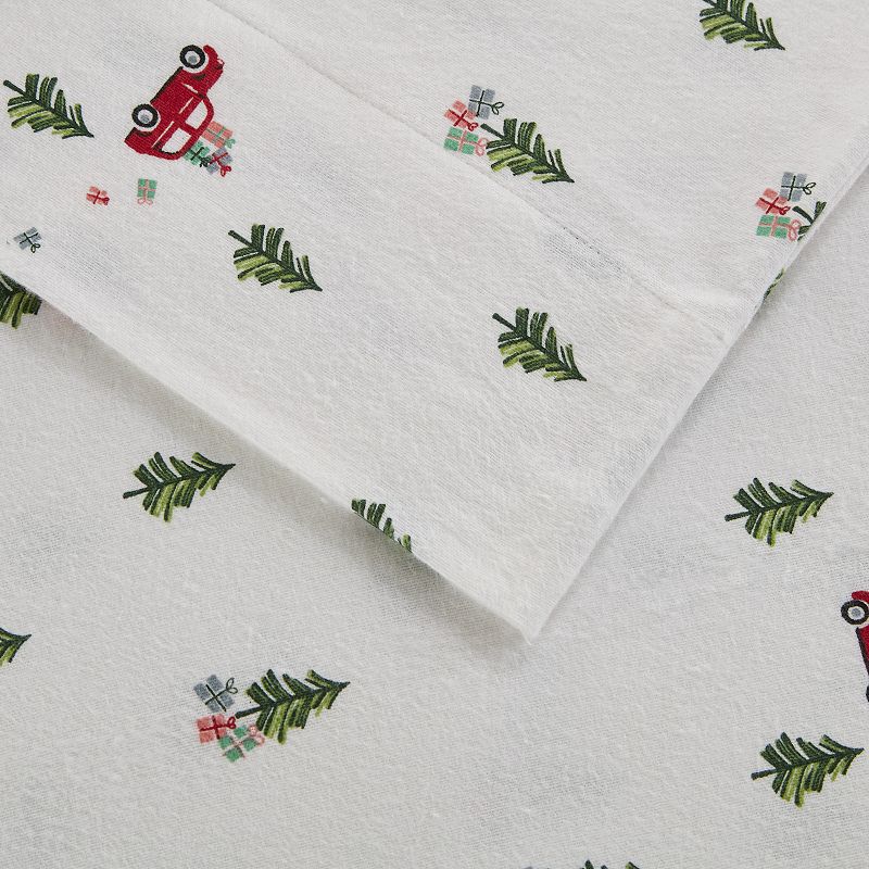 White flannel sheets with a Christmas-themed pattern featuring green pine branches and red trucks with trees.