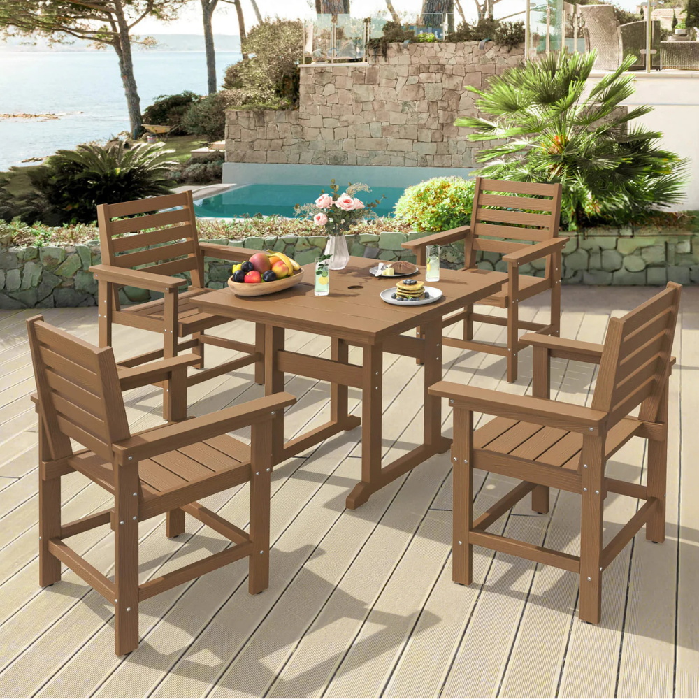 Outdoor patio set with a rectangular wooden table and four matching chairs overlooking a pool and garden. The table holds a vase with flowers and a plate of fruit.
