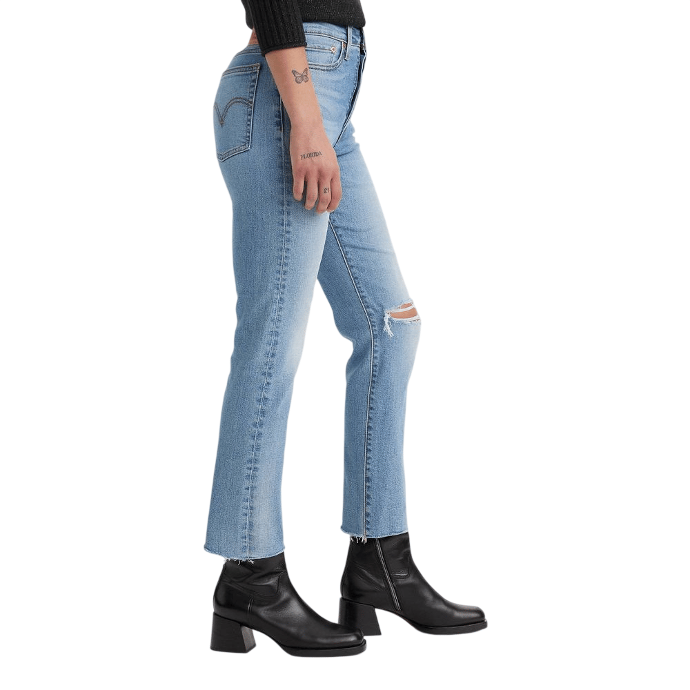 A person is wearing light blue ripped jeans paired with black ankle boots with a block heel.