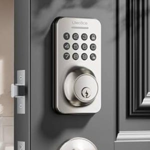 A silver smart lock with a keypad and key slot is installed on a gray door. The keypad features numbers 0-9 and a lock button below.