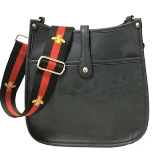 A black leather bag with a decorative strap featuring red and black stripes and bee embroidery.