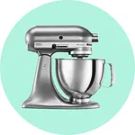 A silver stand mixer with a large stainless steel mixing bowl, set against a light green circle background.