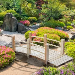 A small wooden bridge is surrounded by lush greenery and vibrant flowers in a serene garden setting.