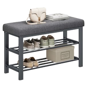 A gray cushioned bench with a metal frame, featuring two slatted shelves for shoe storage, topped with a cream handbag and a stack of books. Beneath, there are three pairs of shoes and a labeled storage box.