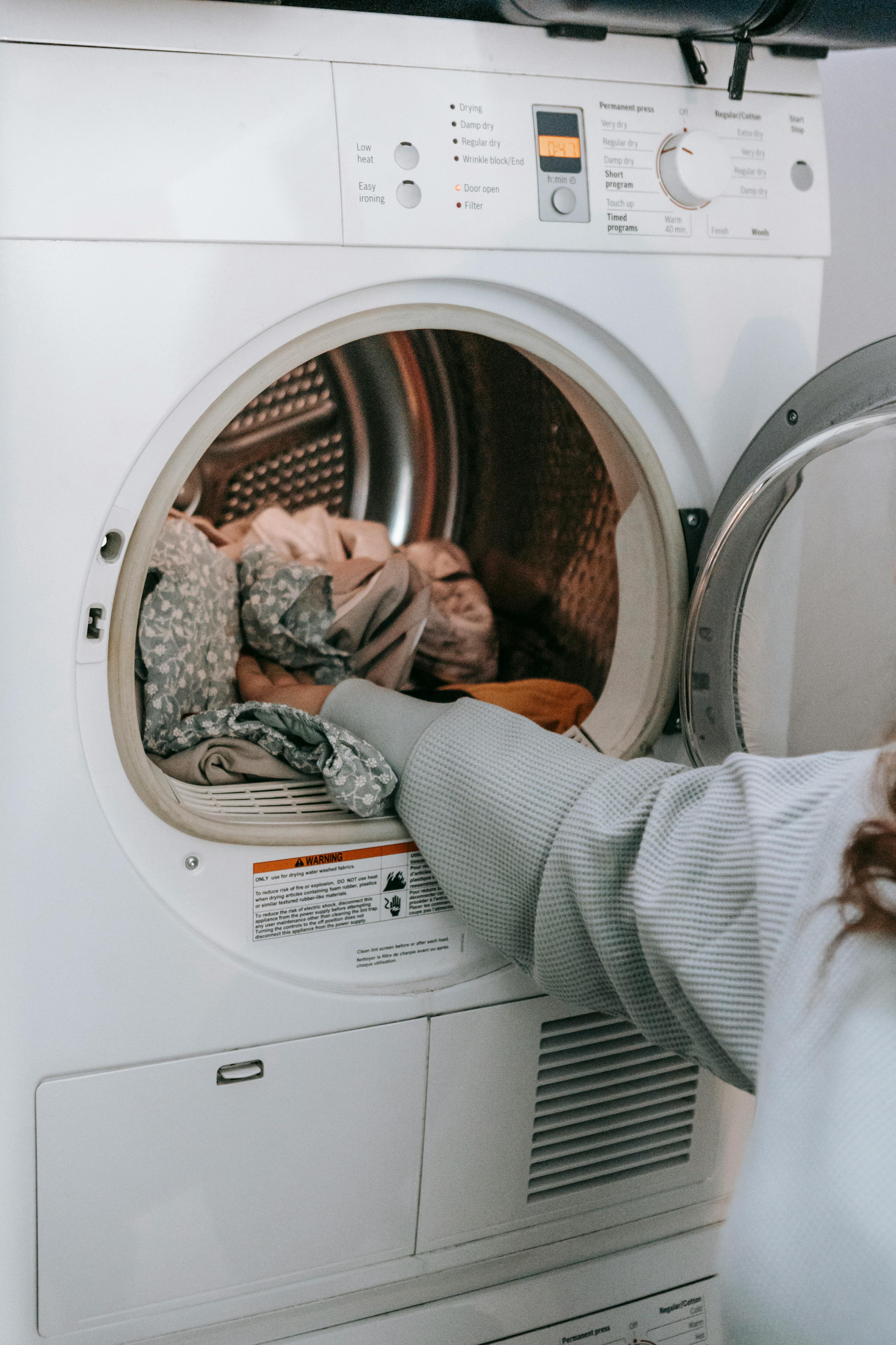 A person is loading laundry into a white clothes dryer.