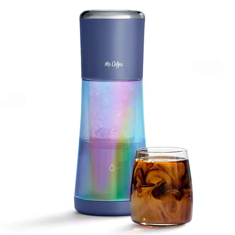 A Mr. Coffee iced coffee maker with a gradient design is next to a glass of swirled coffee, showcasing cold brew preparation.