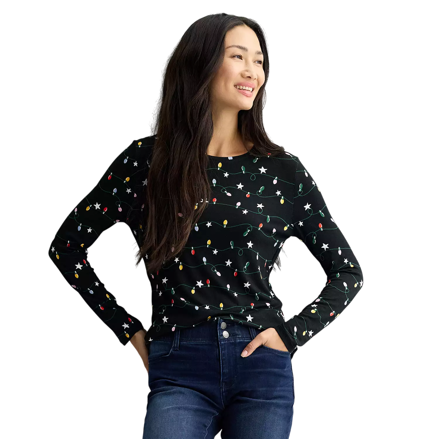 A woman wearing a black long-sleeve shirt with a festive light string pattern and dark blue jeans is standing and smiling.