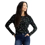 A woman wearing a black long-sleeve shirt with a festive light string pattern and dark blue jeans is standing and smiling.