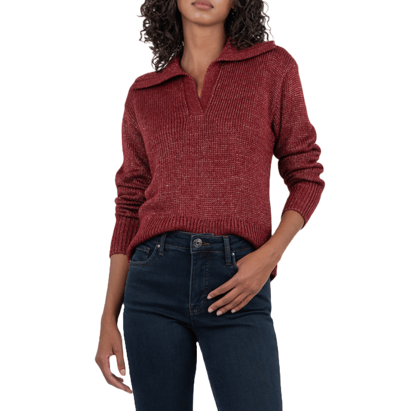 A woman wears a red Henley sweater with a ribbed texture, featuring a collar and a V-neck, paired with dark blue jeans.