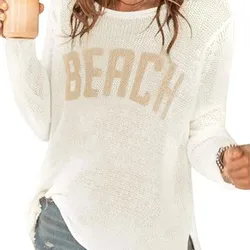 Woman wearing a white knit sweater with \“BEACH\“ text and distressed denim shorts, holding a beverage.