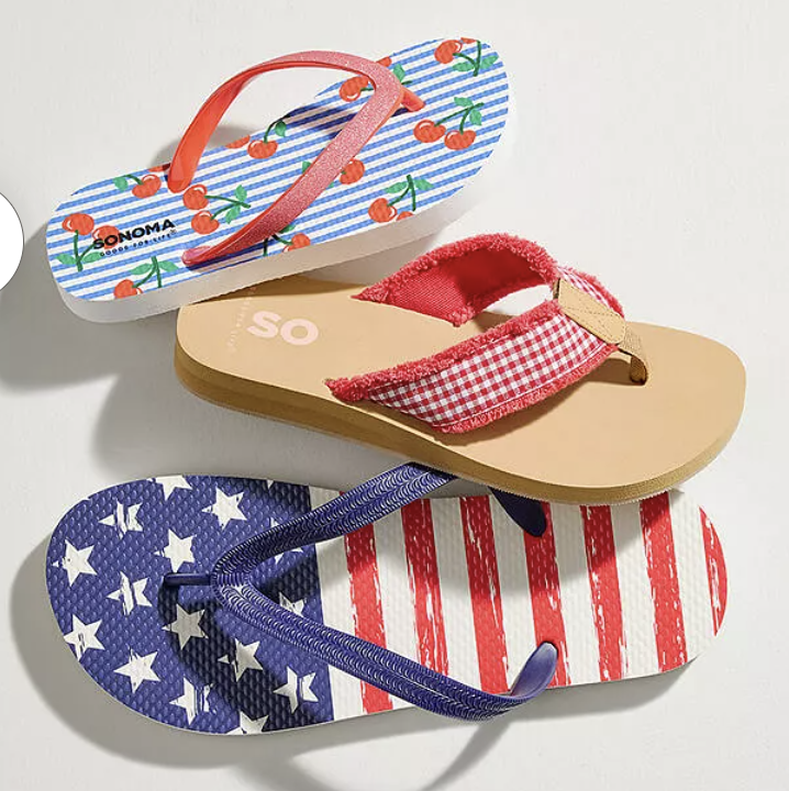 Three pairs of flip-flops with different designs: one features cherries on blue and white stripes, another has a red gingham pattern with a beige sole, and the last displays an American flag motif with stars and stripes.