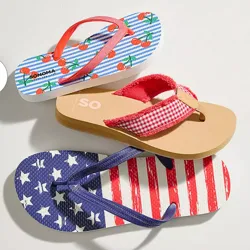 Three pairs of flip-flops with different designs: one features cherries on blue and white stripes, another has a red gingham pattern with a beige sole, and the last displays an American flag motif with stars and stripes.