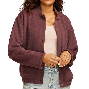 A woman wears a textured, button-up maroon jacket over a light beige top and light blue jeans. She has several rings on her fingers.