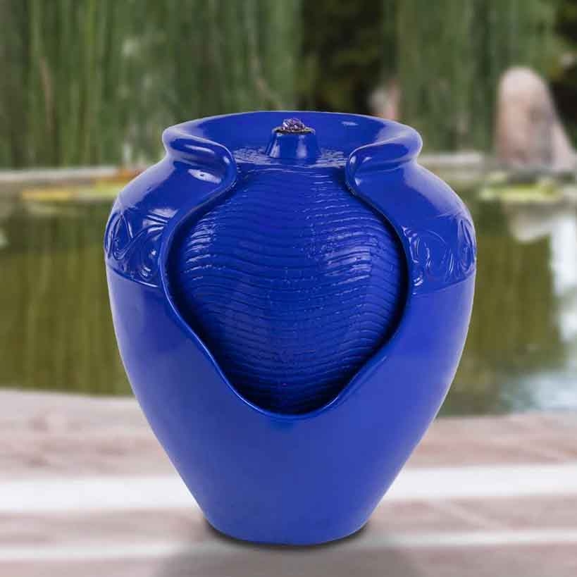 A blue ceramic vase featuring a unique design with a central textured element and open sides, placed against a blurred outdoor background.
