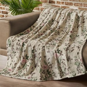 Floral-patterned blanket draped over a brown sofa, set against a brick wall and wooden floor, with a green plant in the background.
