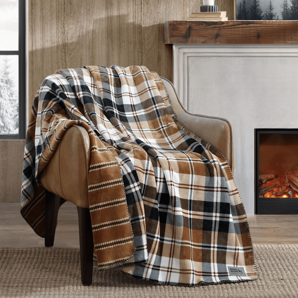 Plaid blanket draped over a brown armchair beside a fireplace, with a snowy outdoor scene through the window.