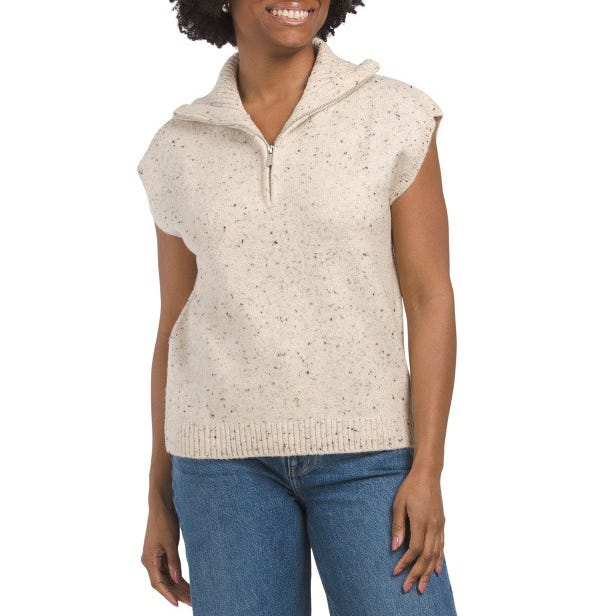 Sleeveless beige knit top with speckled pattern, featuring a half-zip collar. Paired with blue jeans.