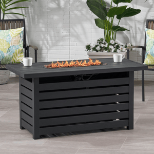 Outdoor patio scene featuring a rectangular black fire pit table with open flames and two chairs with colorful leaf-patterned cushions, surrounded by green and white plants.