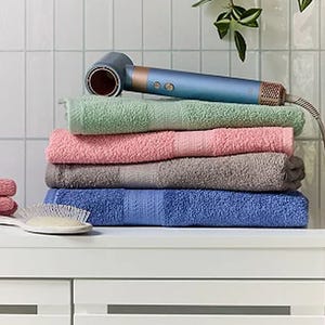 Stack of colorful towels with a blue hairdryer on top and a white hairbrush beside them on a bathroom countertop.