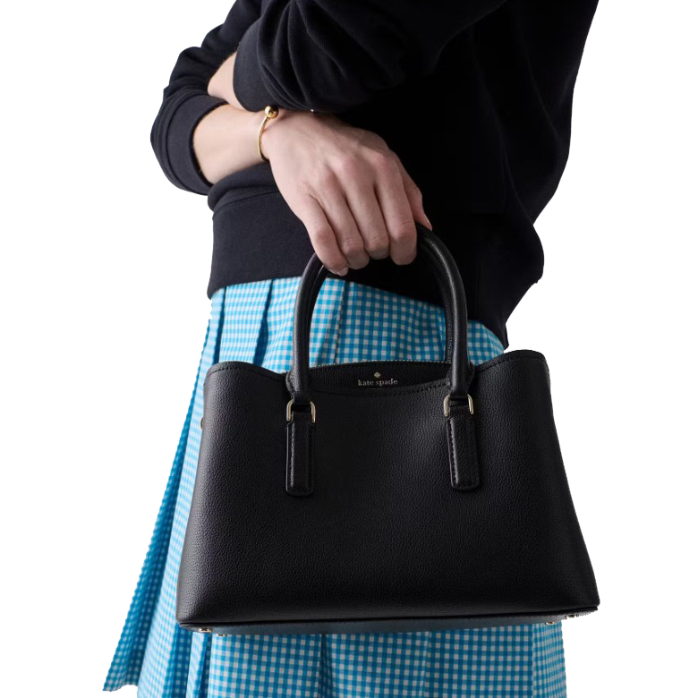 Black Kate Spade handbag with dual handles, paired with a blue gingham skirt and a black sweater.