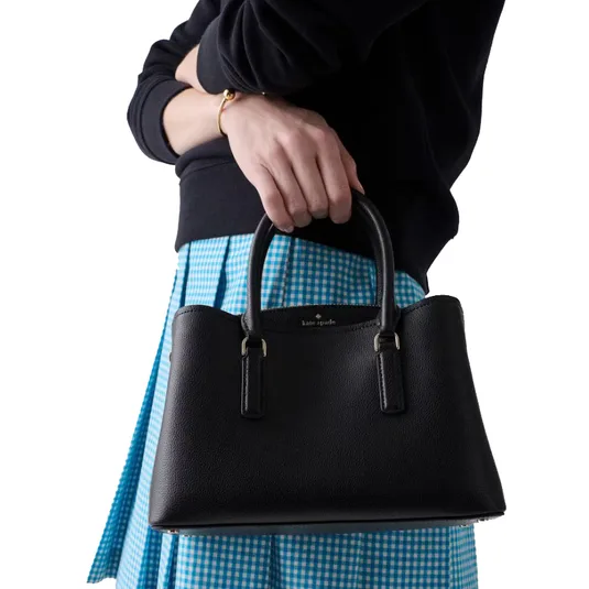Black Kate Spade handbag with dual handles, paired with a blue gingham skirt and a black sweater.