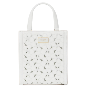 White handbag with floral cutout design and a small \“Kate Spade New York\“ label on the front.