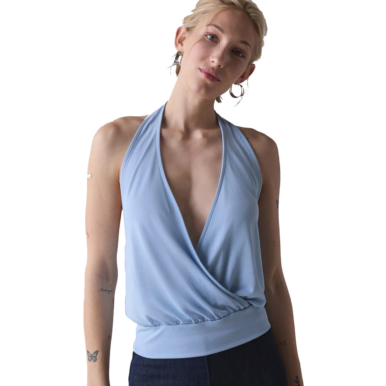 A person is wearing a light blue halter top with a deep V-neck and a gathered hem, paired with dark pants.