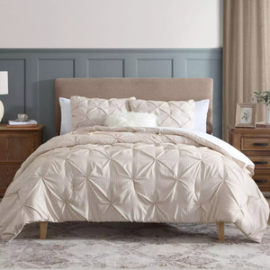 A bedroom setting with a beige tufted bed, striped comforter, and large pillows, flanked by two wooden nightstands with lamps and decor. The wall features paneled molding in gray-blue, and there's a patterned rug beneath the bed.