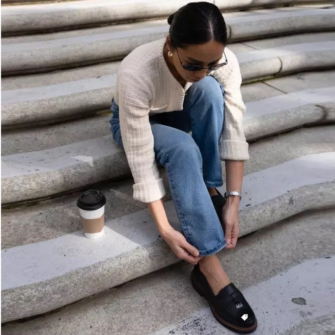 Black loafers with a prominent metallic buckle detail on the upper and a chunky sole. The shoes have a slip-on design.