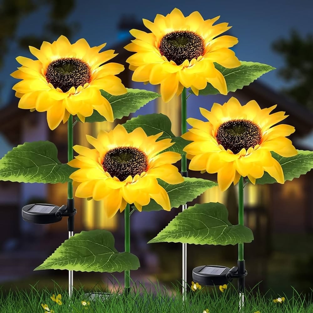 Four solar-powered LED garden lights shaped like sunflowers with vibrant yellow petals and green leaves, each featuring a solar panel for energy. They are designed to illuminate outdoor spaces, providing decorative lighting.