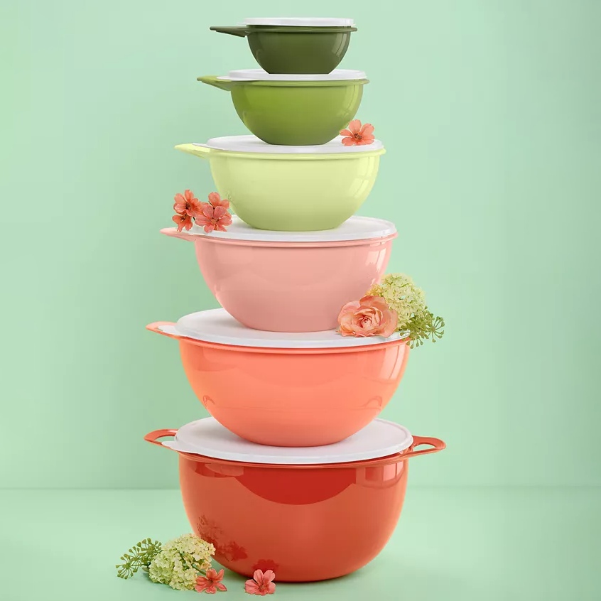 A stack of colorful food storage containers ranging from red to green, with floral accents, each with a lid, set against a green background.