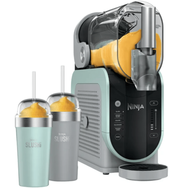 A Ninja slushie maker with a teal and black finish is shown alongside two slushie cups, one in teal and the other in gray, both filled with an orange slushie and topped with straws.