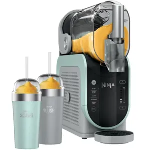 A Ninja slushie maker with a teal and black finish is shown alongside two slushie cups, one in teal and the other in gray, both filled with an orange slushie and topped with straws.