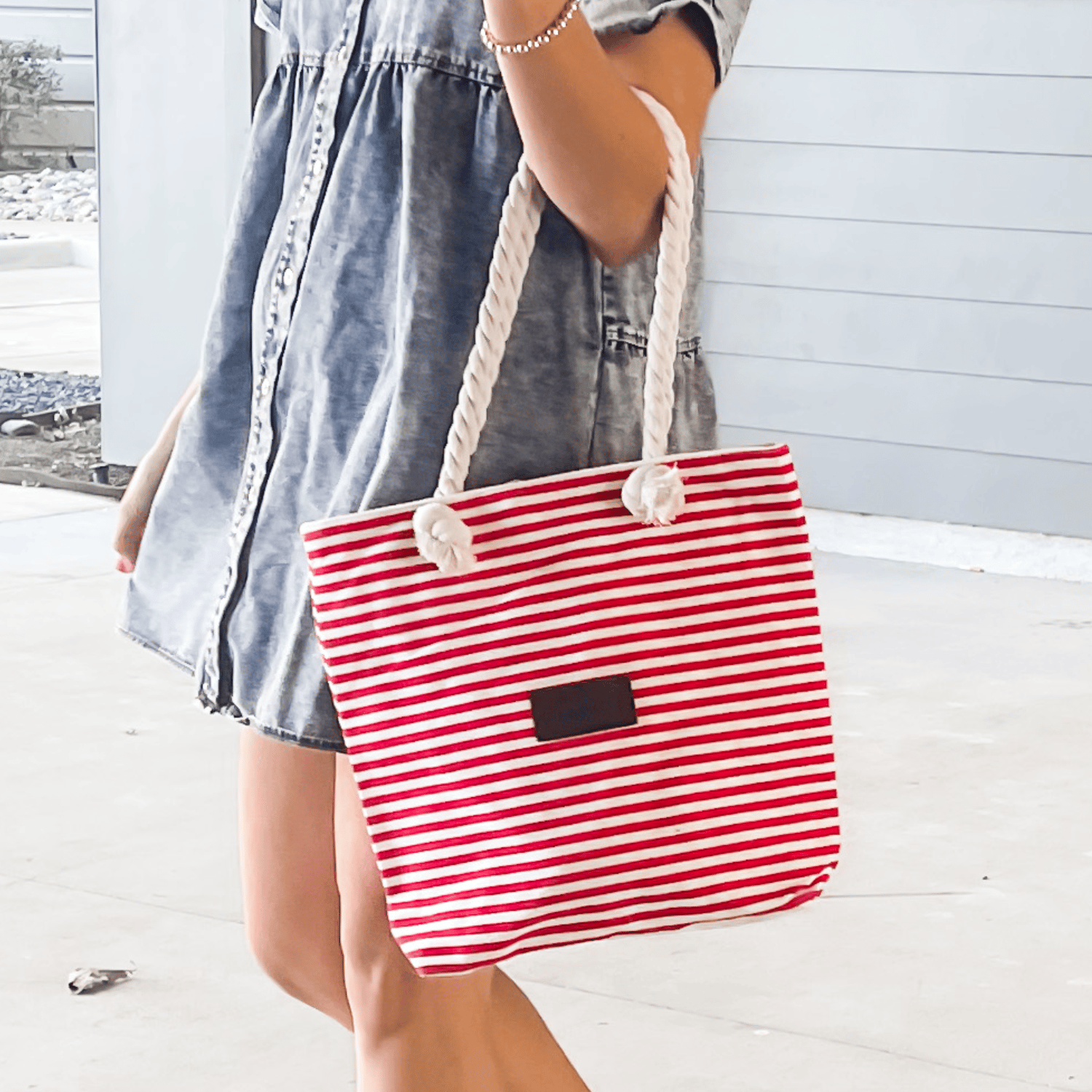 A red and white striped canvas tote with rope handles, featuring a small black rectangular patch on the front.