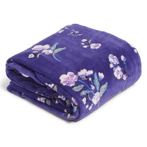 A purple Vera Bradley oversized fleece throw with a floral pattern featuring pink and white flowers with green leaves, offering a cozy and decorative addition to your space.