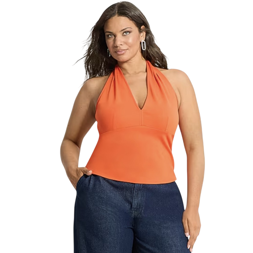 A woman is wearing an orange halter top paired with dark blue jeans. She has long hair and accessorizes with silver hoop earrings.