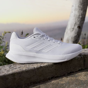 A single white athletic shoe with a textured sole and three stripe design on the side, perched on a stone ledge outdoors.