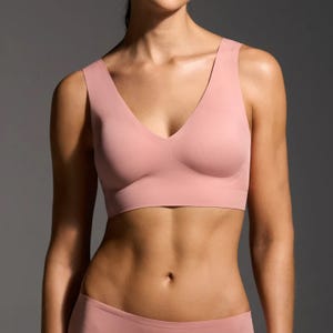 Woman wearing a pale pink sports bra, with a V-neckline and wide straps.