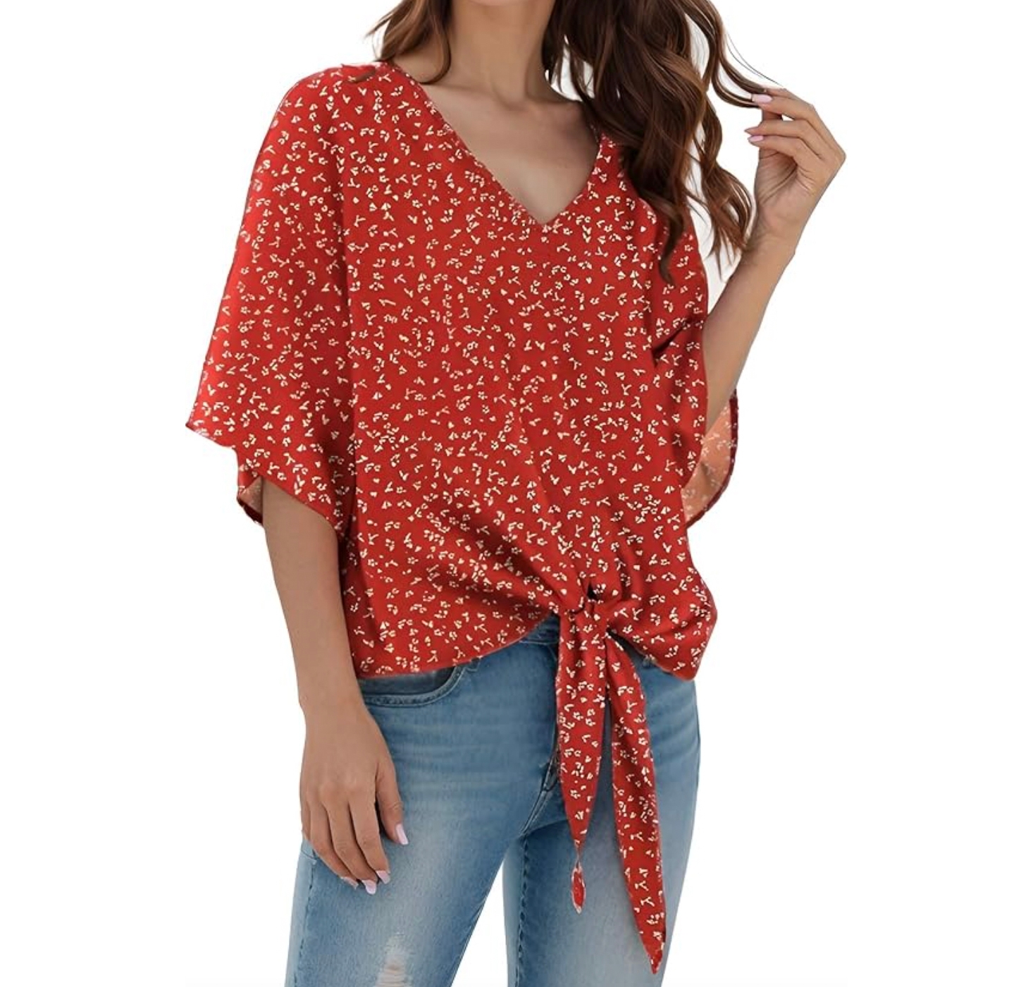 A red, floral-patterned blouse with short sleeves features a V-neckline and a front tie detail, paired with light blue denim jeans.