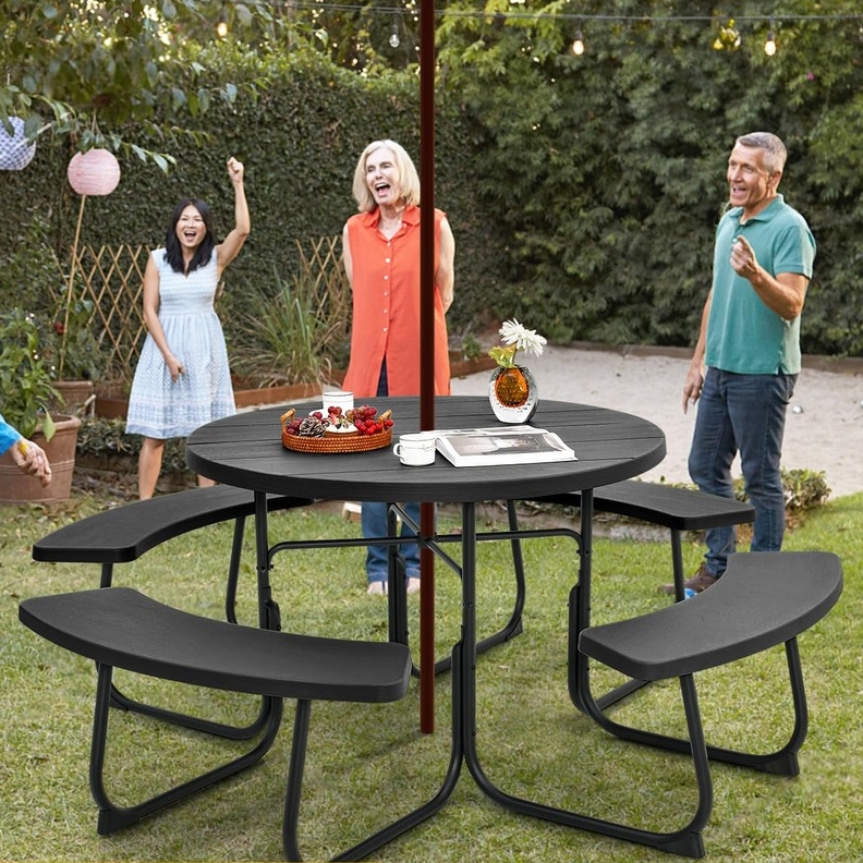 A round outdoor table with attached bench seats, surrounded by three people enjoying a garden setting.